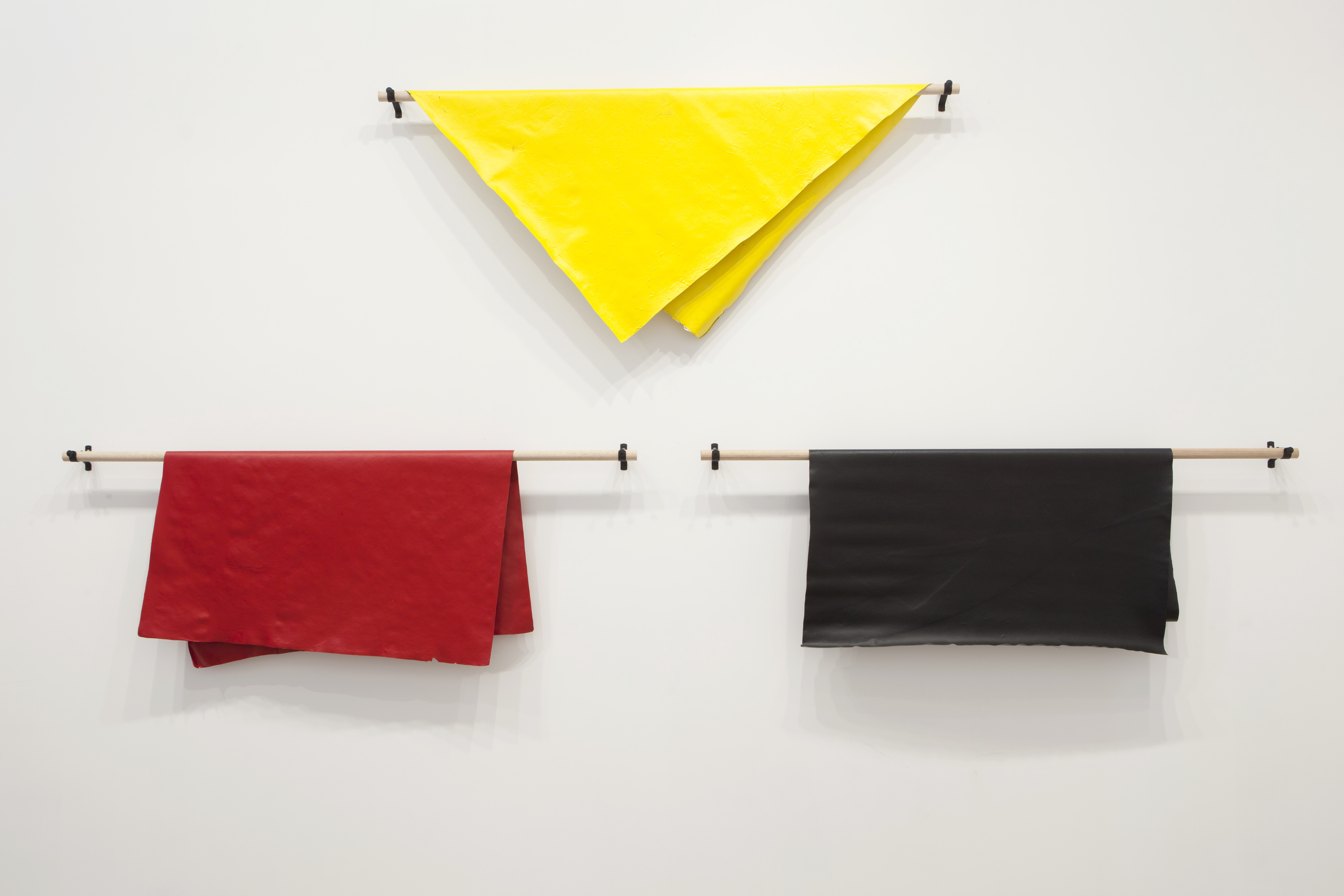 Three pieces of acrylic material in yellow, red and black hanging from sections of wooden dowel.