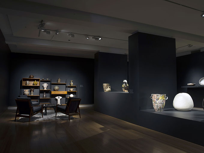 Installation view of sitting room with tables/chairs and ceramics on shelves at QUT Art Museum