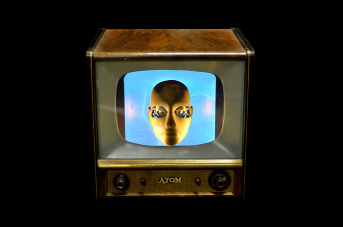 Image of old fashioned TV with a picture of a manikin’s face on a blue screen on a black background