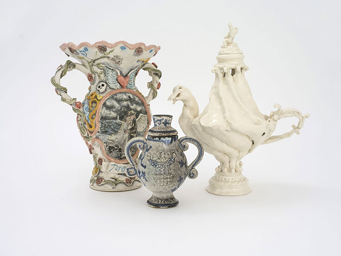 Image of three vases – one large vase with a picture of a man and woman with of decorative flowers, one small blue/grey vase with a picture of a man, one white vase in the shape of a duck