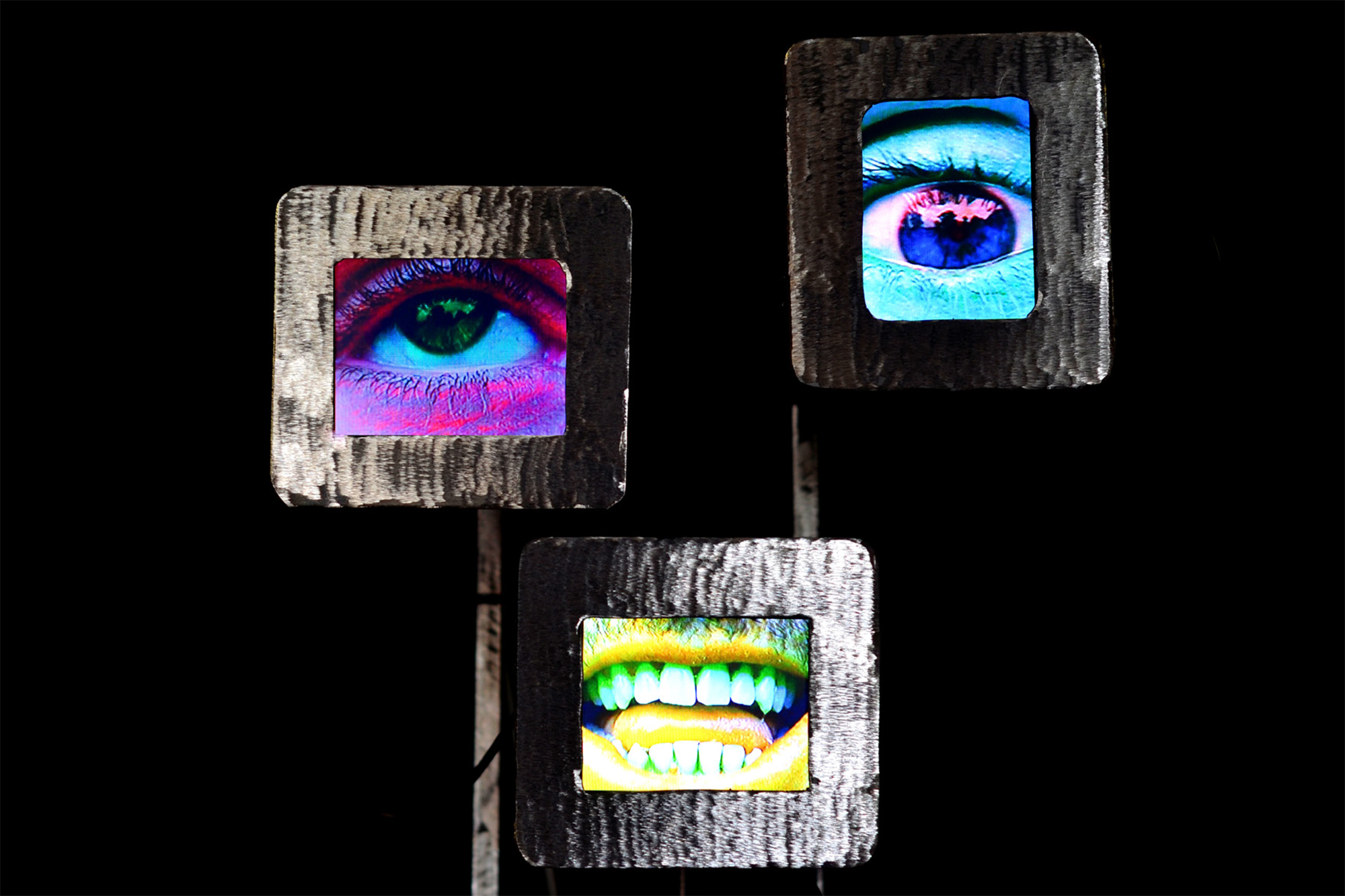 Abstract artwork of a robot with three screens – one with picture of a pink eye, one with picture of a blue eye and one with picture of a yellow mouth on a black background