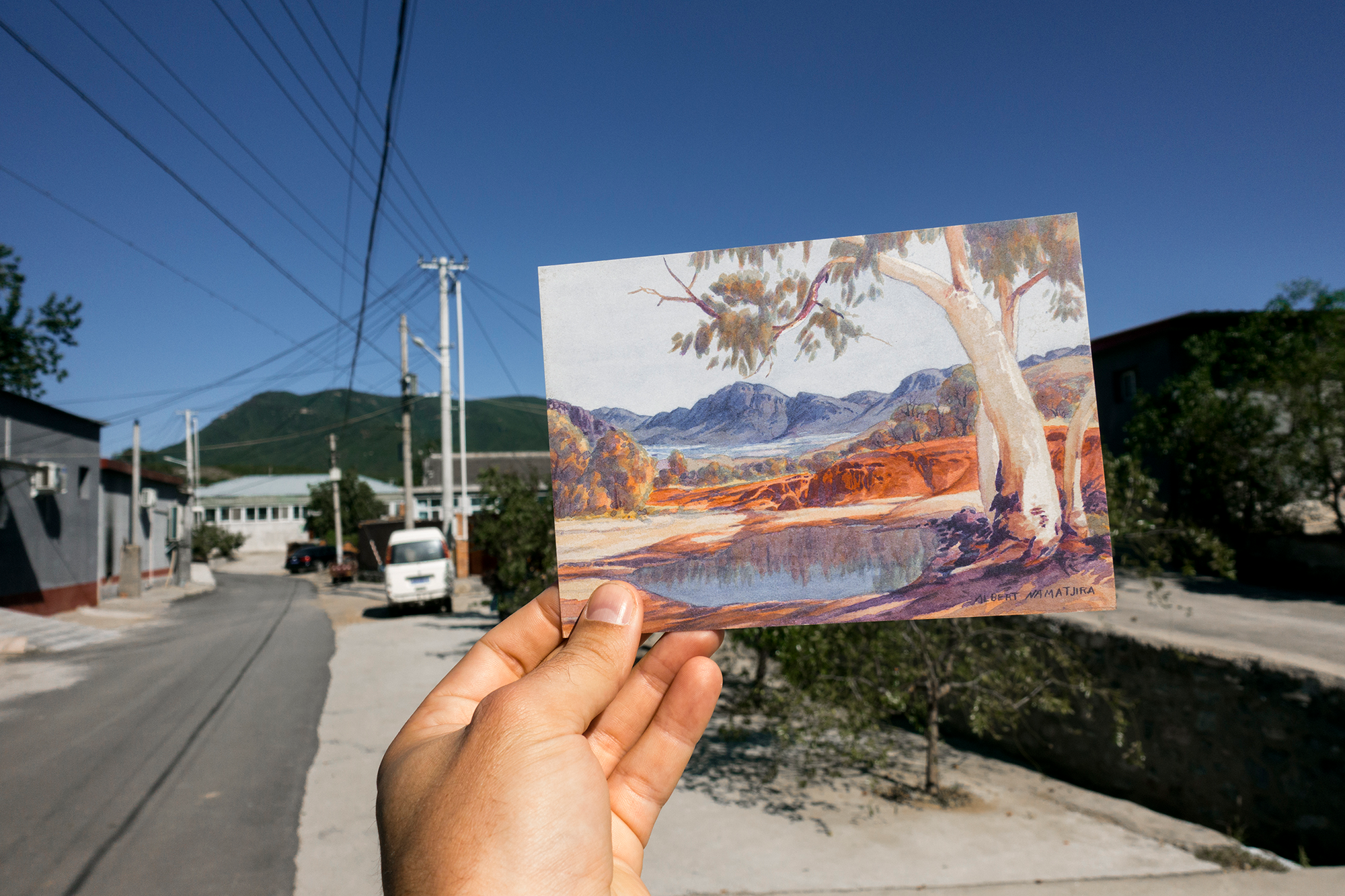 Image of person holding a photo of a mountain landscape alongside a road