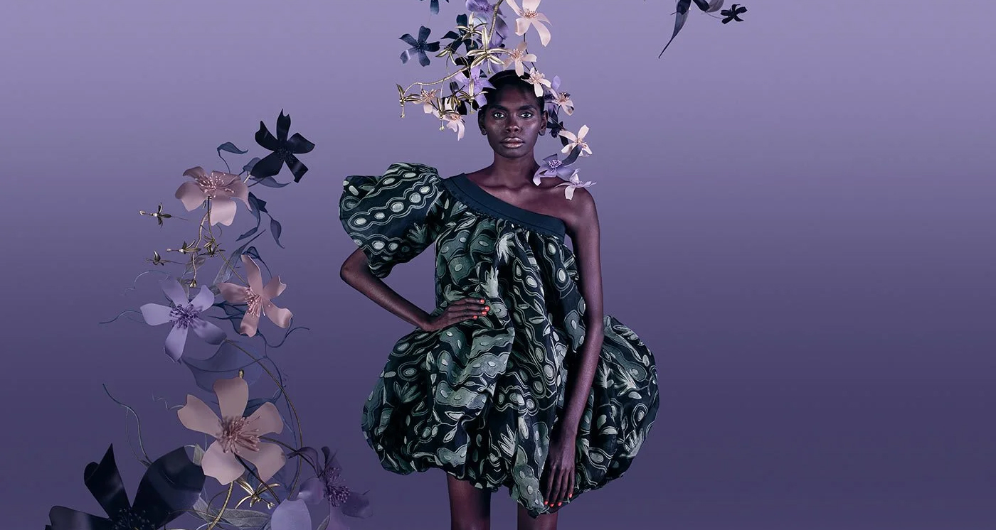 Model wearing one-shouldered, voluminous dress depicting seedpods, surrounded by flowers