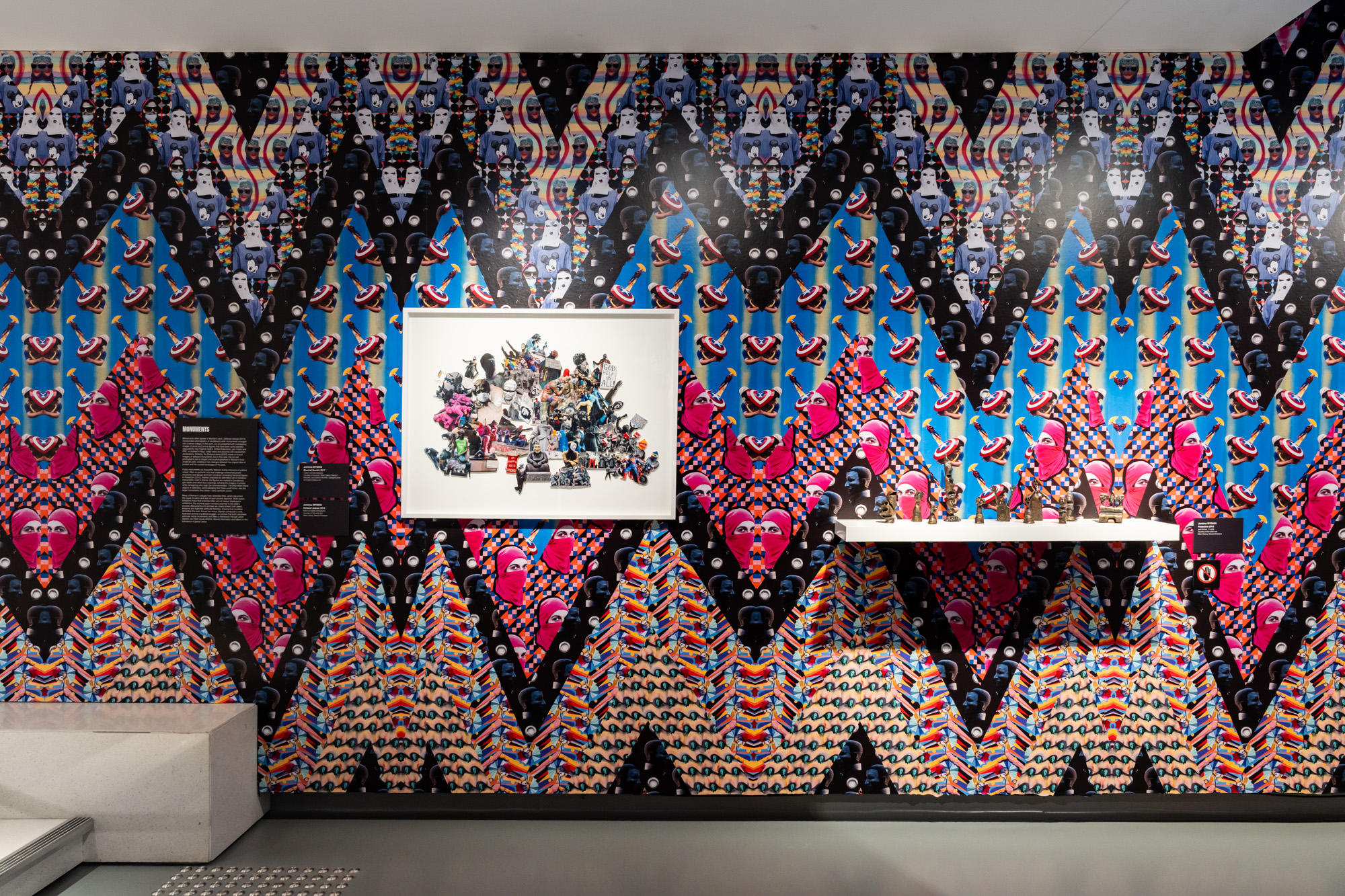 Framed collage and bronze sculptures on a gallery wall with brightly patterned wallpaper