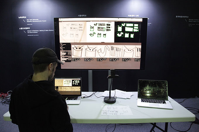 Image of man standing at desk with two laptops and a large projector screen on the wall