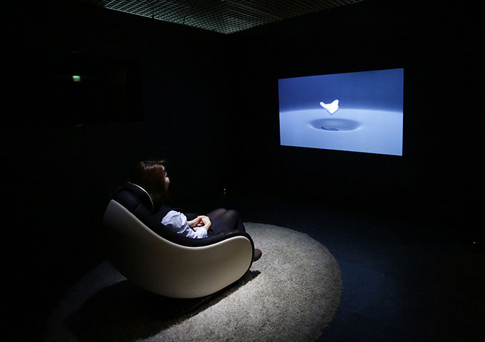 Image of lady sitting in a chair in a dark room looking at a projector screen on the wall