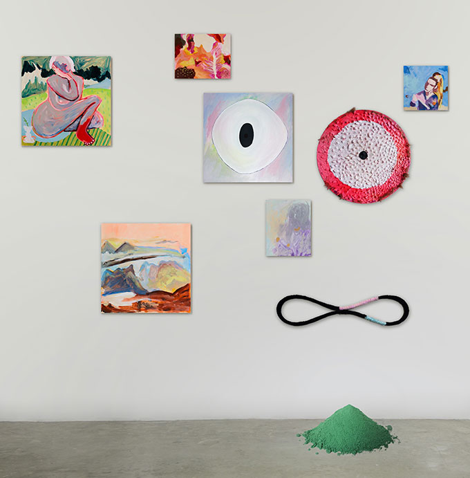 Painting of eight artworks on a white wall with green mound of paint on the ground